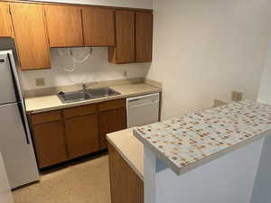 Kitchen featuring a peninsula, freestanding refrigerator, light countertops, and dishwasher