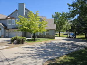 View of front facade featuring driveway, stone siding, a shingled roof, and stucco siding
