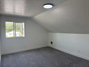 Bonus room with dark carpet and lofted ceiling