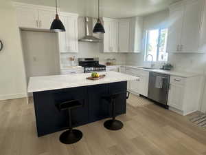 Kitchen featuring wall chimney exhaust hood, appliances with stainless steel finishes, a center island, white cabinetry, and a kitchen bar