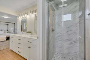 Ensuite bathroom with a marble finish shower, double vanity, and wood finished floors
