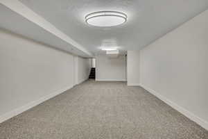 Finished basement featuring a textured ceiling, carpet flooring, and stairway