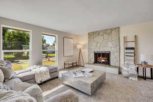 Carpeted living room featuring a stone fireplace and baseboards