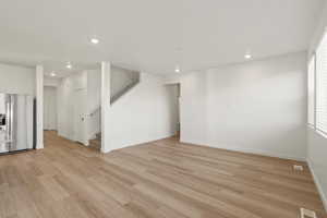 Basement with stainless steel fridge with ice dispenser, light wood finished floors, recessed lighting, and stairs