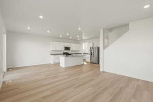 Kitchen featuring recessed lighting, white cabinetry, stainless steel appliances, a kitchen island with sink, and light wood-style flooring