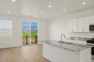 Kitchen featuring light stone countertops, stainless steel appliances, white cabinets, recessed lighting, and light wood-style flooring