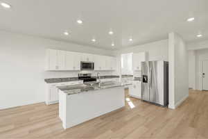 Kitchen featuring appliances with stainless steel finishes, white cabinetry, recessed lighting, dark stone counters, and light wood-type flooring