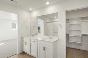 Bathroom featuring double vanity, a shower stall, light colored carpet, a walk in closet, and recessed lighting