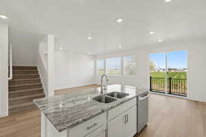 Kitchen with light stone counters, light wood-type flooring, white cabinets, recessed lighting, and an island with sink