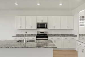 Kitchen with white cabinetry, light stone countertops, appliances with stainless steel finishes, light wood finished floors, and recessed lighting