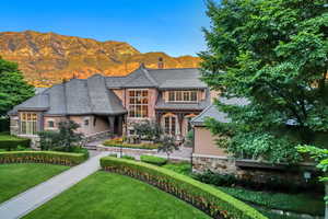 View of front facade featuring stone siding, a mountain view, stucco siding, a front lawn, and a chimney