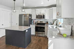 Kitchen featuring appliances with stainless steel finishes, dark wood-type flooring, white cabinets, light stone counters, and tasteful backsplash