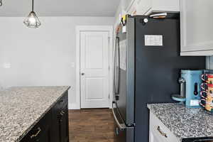 Kitchen with dark wood-style flooring, white cabinetry, light stone counters, freestanding refrigerator, and decorative light fixtures