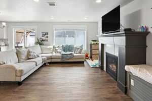 Living room with a textured ceiling, healthy amount of natural light, a fireplace, dark wood finished floors, and recessed lighting