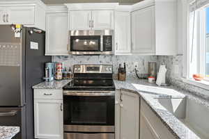 Kitchen featuring stainless steel appliances, tasteful backsplash, and white cabinetry