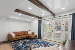 Living area with large exterior patio doors, wood looking LVP floors, recessed lighting, and beam ceiling.