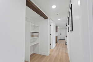 Hallway featuring light wood-type flooring and recessed lighting, washer and dryer space and shelving.