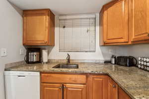 Kitchen with dishwasher, brown cabinetry, and light stone countertops
