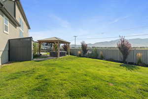 Fenced backyard with a gazebo, a mountain view, a hot tub, and a shed