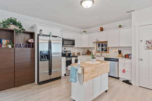 Kitchen with stainless steel appliances, white cabinets, light wood finished floors, and light countertops