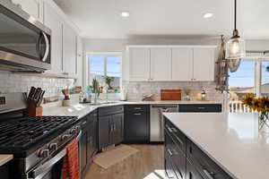 Kitchen featuring stainless steel appliances, white cabinetry, light wood-style flooring, recessed lighting, and decorative light fixtures
