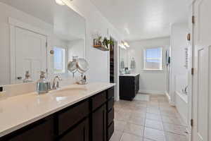 Bathroom with tile patterned floors, two vanities, a shower with door, and a tub