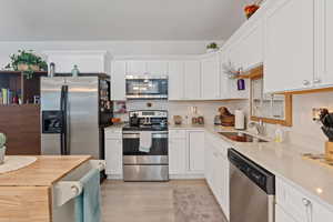 Kitchen with appliances with stainless steel finishes, light wood-type flooring, and white cabinets