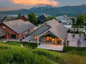 Back of property with a mountain view, stone siding, a patio area, and a shingled roof