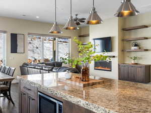 Kitchen featuring a glass covered fireplace, stainless steel microwave, decorative light fixtures, dark brown cabinets, and dark wood-style floors