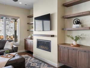 Living room featuring dark wood-style floors, a glass covered fireplace, a ceiling fan, and recessed lighting