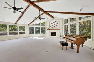 Living area with high vaulted ceiling, beamed ceiling, a brick fireplace, carpet floors, and a ceiling fan
