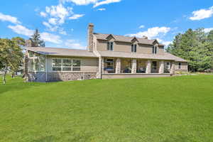 Rear view of property with stone siding, a chimney, a lawn, stucco siding, and a shingled roof