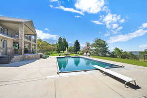 Outdoor pool with a diving board, a mountain view, a patio, and a lawn