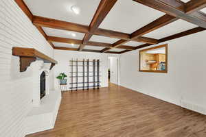 Unfurnished living room with light wood finished floors, a brick fireplace, beam ceiling, and coffered ceiling