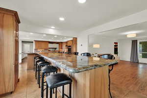 Kitchen with a kitchen breakfast bar, recessed lighting, brown cabinetry, light tile patterned floors, and dark stone countertops