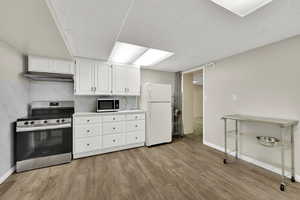 Kitchen with stainless steel appliances, white cabinetry, light wood-style flooring, light countertops, and a drop ceiling