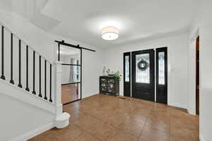 Foyer entrance featuring a barn door, stairway, and tile patterned flooring