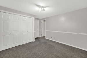 Unfurnished bedroom with dark colored carpet, a textured ceiling, and a closet