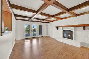 Unfurnished living room with a fireplace, wood finished floors, beam ceiling, coffered ceiling, and brick wall