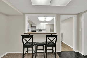Kitchen with a drop ceiling, dark tile patterned floors, a kitchen bar, stainless steel appliances, and white cabinets