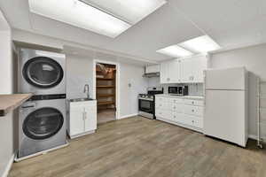 Kitchen featuring stacked washer / drying machine, appliances with stainless steel finishes, a drop ceiling, light wood-style floors, and white cabinetry