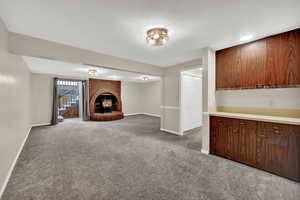 Basement with a brick fireplace, dark colored carpet, stairs, and a textured ceiling