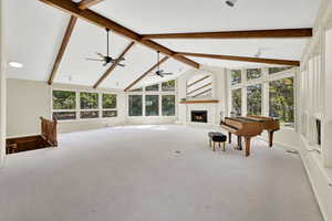 Living area featuring high vaulted ceiling, a brick fireplace, beamed ceiling, carpet flooring, and a ceiling fan