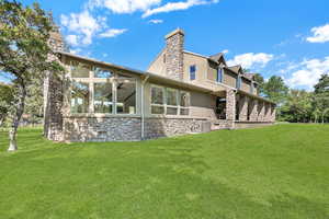 Back of property with a chimney, stone siding, a yard, and stucco siding