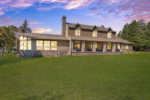 Back of house at dusk with a chimney, stone siding, a lawn, and stucco siding
