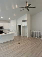 Kitchen featuring white cabinets, vaulted ceiling, a kitchen bar, appliances with stainless steel finishes, and light wood-type flooring