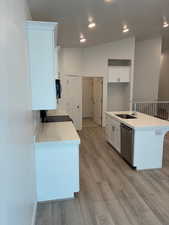 Kitchen with white cabinets, light stone countertops, light wood-style flooring, a center island with sink, and stainless steel dishwasher