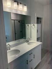 Bathroom with light wood finished floors, a stall shower, and double vanity