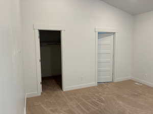Unfurnished bedroom featuring light carpet, a spacious closet, and lofted ceiling