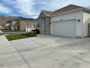 View of side of property with driveway, stone siding, a residential view, an attached garage, and roof with shingles